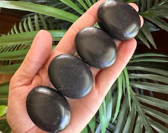 May include: Four smooth, oval-shaped black stones arranged in a line. Each stone has a polished, dark surface with a consistent matte finish. The stones are uniform in size and shape, displaying a deep, solid black color throughout their structure.