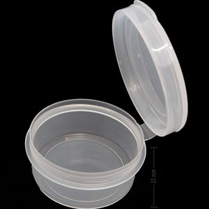 May include: A clear plastic container with a hinged lid. The container is 35 mm in diameter and 15 mm in height.