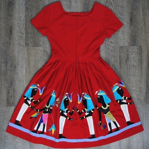 May include: A red dress with a scoop neck and short sleeves. The dress has a pleated skirt with embroidered figures of people in blue and white.