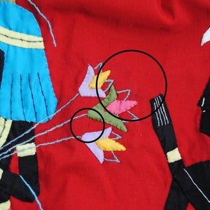 May include: A red fabric panel with two embroidered figures in black, blue, and yellow. The figures are holding a bouquet of colorful flowers.