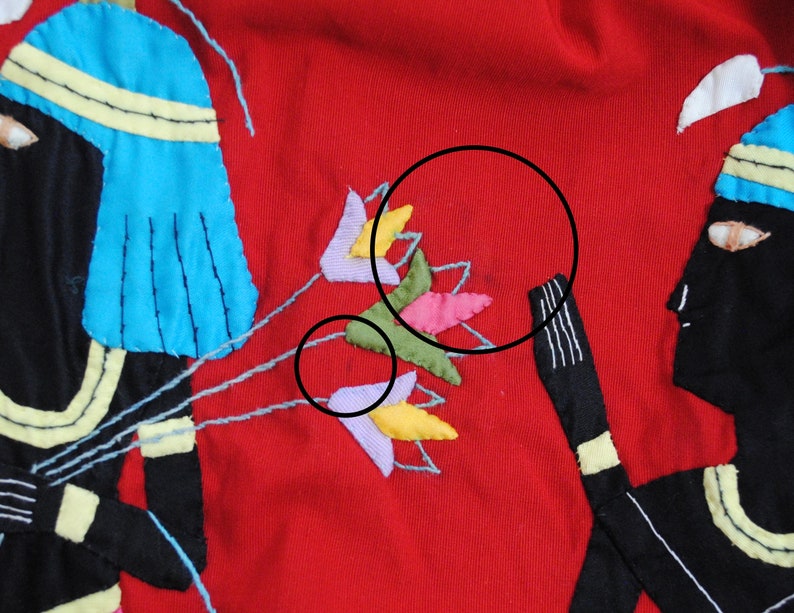 May include: A red fabric panel with two embroidered figures in black, blue, and yellow. The figures are holding a bouquet of colorful flowers.