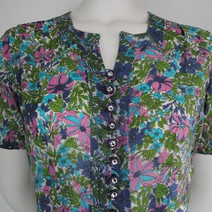 May include: A white, blue, green, and pink floral print short-sleeved button-up shirt with a v-neck.