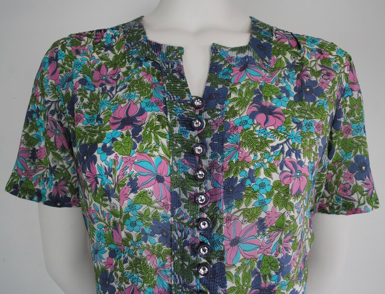 May include: A white, blue, green, and pink floral print short-sleeved button-up shirt with a v-neck.