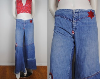 May include: Blue denim bell bottom pants with red stitching and star-shaped patches. The pants have a high waist and a wide leg.