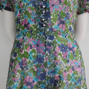 May include: A vintage dress with a floral print in shades of pink, blue, and green. The dress has a button-up front and short sleeves.