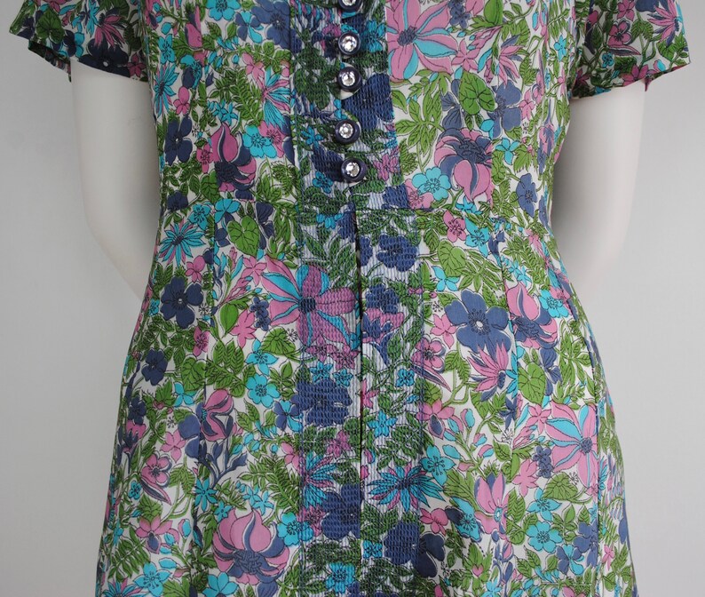 May include: A vintage dress with a floral print in shades of pink, blue, and green. The dress has a button-up front and short sleeves.