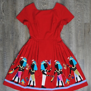 May include: A red dress with a square neckline and short sleeves. The skirt of the dress is decorated with an embroidered design of figures in blue, white, and black.