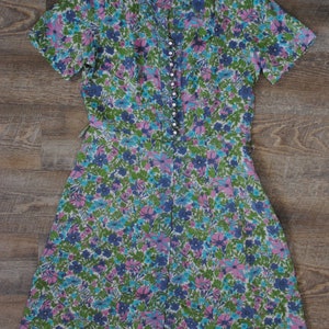 May include: A vintage floral dress with a V-neckline and short sleeves. The dress is made of a lightweight fabric and has a button-up front.