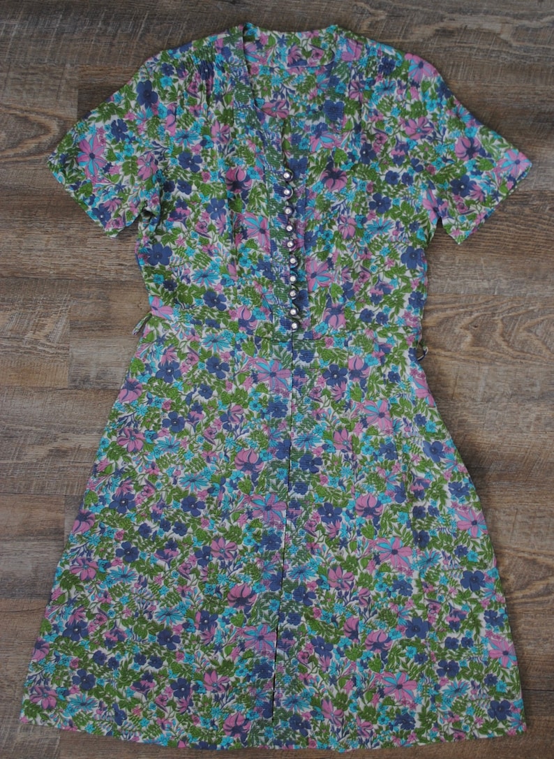 May include: A vintage floral dress with a V-neckline and short sleeves. The dress is made of a lightweight fabric and has a button-up front.