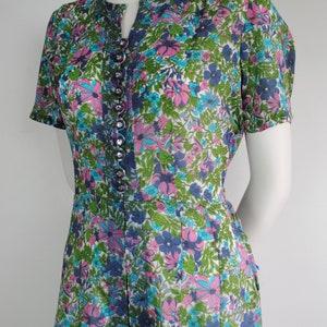 May include: A vintage floral print dress with a button-up front and short sleeves. The dress is white with pink, blue, and green flowers.