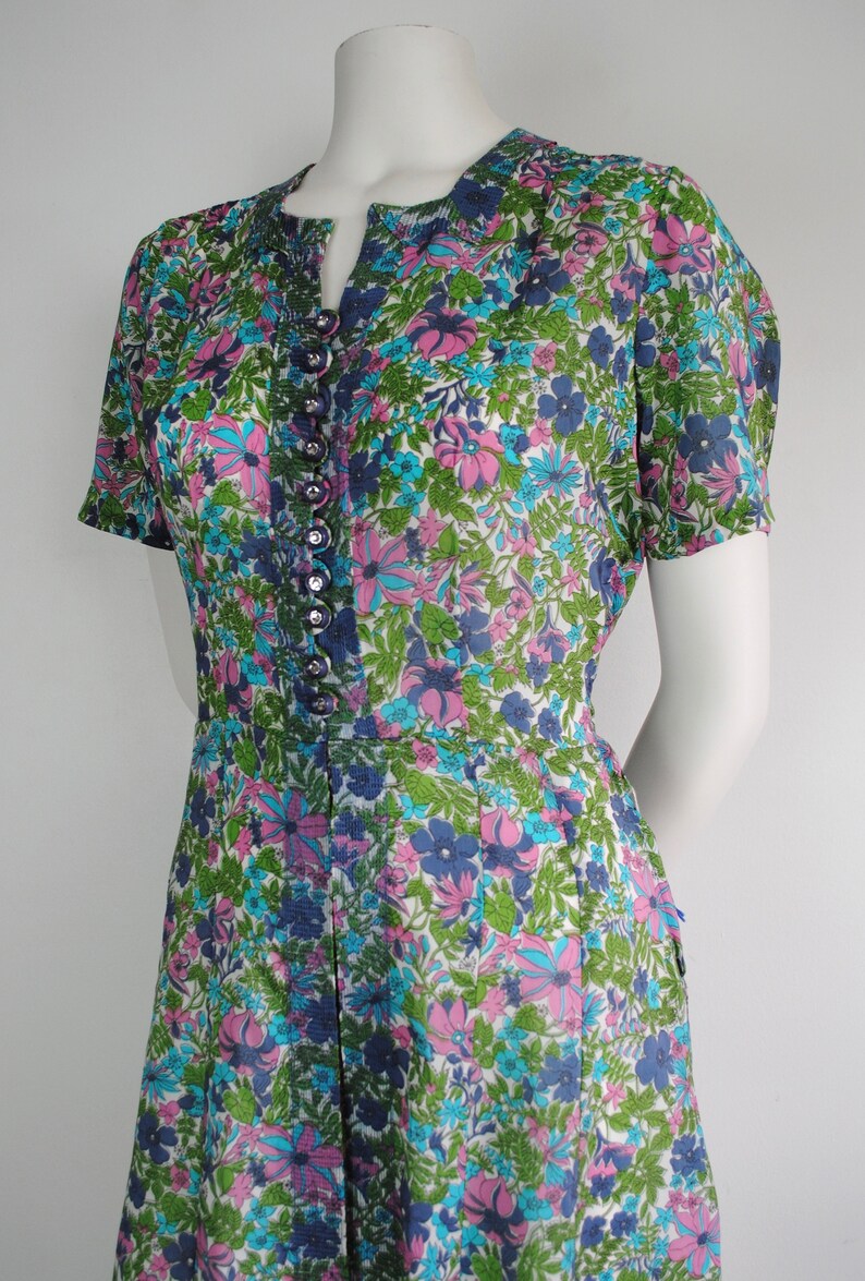 May include: A vintage floral print dress with a button-up front and short sleeves. The dress is white with pink, blue, and green flowers.