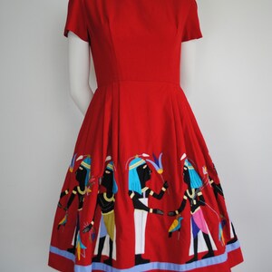 May include: A red vintage dress with a fitted bodice and a full skirt. The skirt features an embroidered design of figures in a procession, with blue, yellow, and white accents.