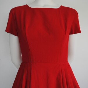 May include: A red vintage dress with a fitted bodice and a full skirt. The dress has a scoop neckline and short sleeves.