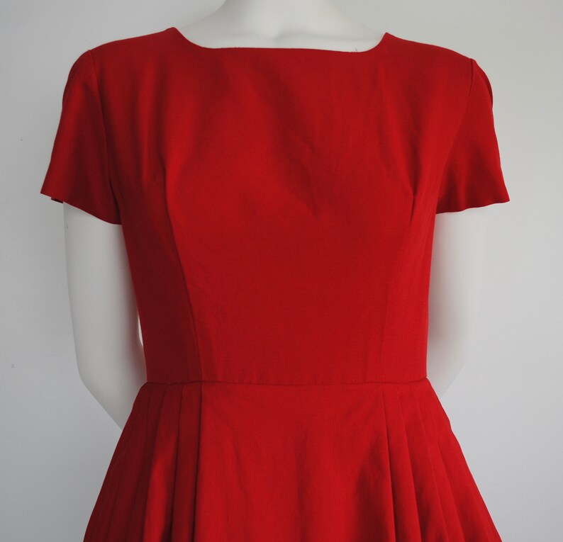 May include: A red vintage dress with a fitted bodice and a full skirt. The dress has a scoop neckline and short sleeves.