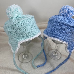 May include: Two crocheted hats with pom-poms. One hat is light blue with a white trim and the other is light green with a white trim.