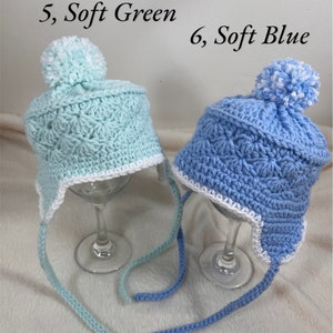 May include: Two crocheted hats with white pom-poms. The hat on the left is light blue and the hat on the right is light green. Both hats have white trim around the brim and are tied with long strings.
