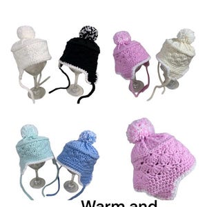 May include: Six crocheted baby hats with pom-poms. The hats are in various colors, including white, black, pink, light blue, and a darker blue. The hats have ear flaps and are tied with a string under the chin.