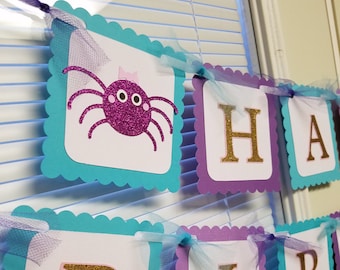 May include: Purple, teal, and white banner with scalloped edges and gold glitter letters spelling "Happy Birthday". The first banner features a pink glitter spider with white eyes.