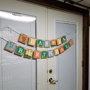 May include: A banner with the words "Happy Birthday" in colorful letters with jungle animal illustrations. The banner is strung across two white doors with blinds.