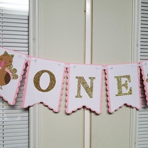 Pu&ograve; includere: Striscione rosa e bianco con lettere dorate glitter che compongono la parola "ONE" e due illustrazioni di tacchini marroni e rosa alle estremit&agrave;.