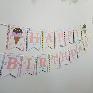 May include: A pink, yellow, and blue Happy Birthday banner with ice cream cone accents. The banner is made of cardstock and has a scalloped edge.
