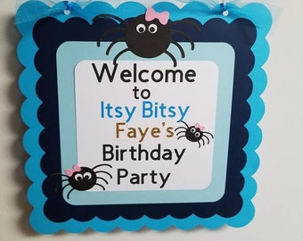 May include: Welcome to Itsy Bitsy Faye's Birthday Party sign with a blue and white background and black spiders with pink bows.
