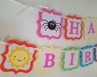 May include: A colorful Happy Birthday banner with a sun, spider, and letters. The banner is made of paper and has a white background.