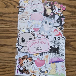 May include: A collection of cat-themed stickers featuring various cartoon cats in different poses. Some stickers include text like "TICKET", "Admit One to The Cats' Meow", and "BINGO" with numbers. The stickers are colorful and playful.