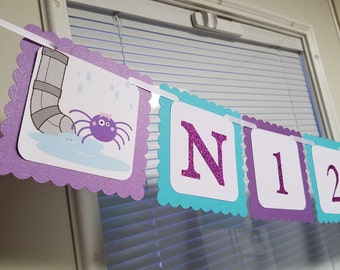 May include: Purple and teal banner with a spider, raindrops, and the letters N12. The banner is made of cardstock and has a scalloped edge.