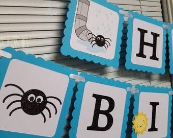 May include: A blue and white banner with the words "Happy Birthday" spelled out. Each letter is on a separate square with a blue border. The squares have a scalloped edge. There are also images of spiders and a sun on the banner.
