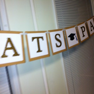 May include: A brown and white banner with gold letters spelling "Congrats" and a black graduation cap with a blue tassel.