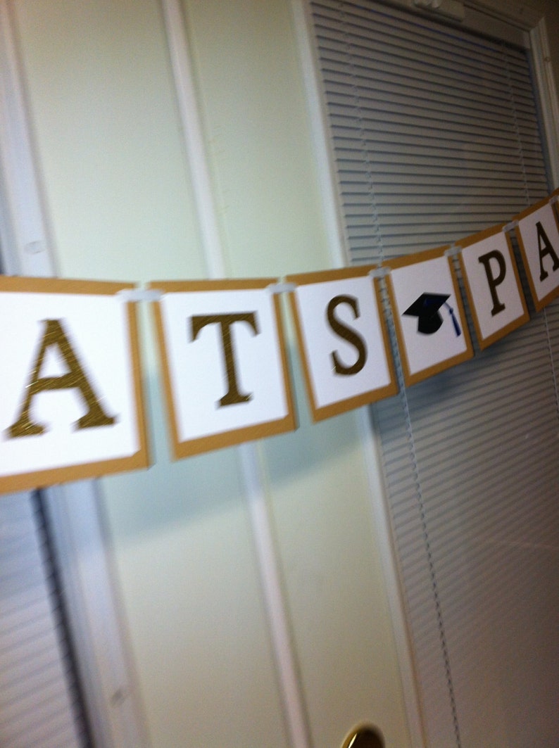 May include: A brown and white banner with gold letters spelling "Congrats" and a black graduation cap with a blue tassel.