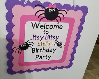 May include: Purple and pink welcome sign with a scalloped border. The sign says "Welcome to Itsy Bitsy Stella's Birthday Party" with three black spiders with pink bows.