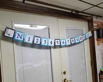 May include: A blue and white banner with the letters N and numbers 1 through 12. The banner is decorated with a small spider and a sun.
