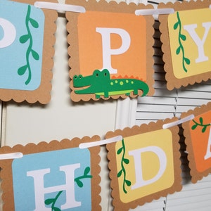 May include: A Happy Birthday banner with brown scalloped edges and white letters. The letters are on different colored squares: blue, orange, yellow, and light blue. Each square has a green vine with leaves. The letter P has a green alligator on it.
