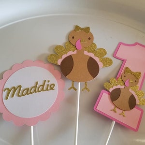Pu&ograve; includere: Tre topper per torta a forma di tacchino rosa e marrone con accenti di glitter dorati. I topper presentano un tacchino con un fiocco rosa, un numero uno e un cerchio con il nome Maddie.