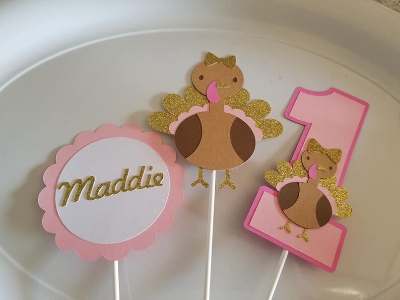 Pu&ograve; includere: Tre topper per torta a forma di tacchino rosa e marrone con accenti di glitter dorati. I topper presentano un tacchino con un fiocco rosa, un numero uno e un cerchio con il nome Maddie.
