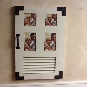 May include: White wooden picture frame with black metal accents and a shutter design. The frame has five openings for photos, each with a different family portrait.