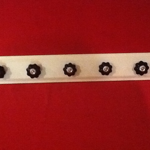 May include: A white wooden coat rack with five black knobs. The knobs are shaped like a flower with a silver center.