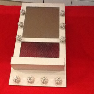 May include: White wooden frame with a mirror and a shelf. The frame is decorated with white ceramic knobs.