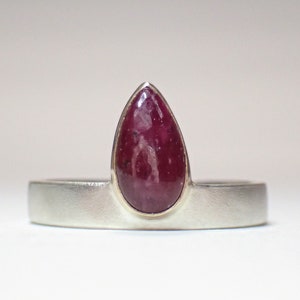 May include: A silver ring with a teardrop-shaped ruby gemstone set in a gold bezel.