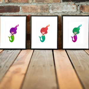 Puede incluir: Tres impresiones enmarcadas de ilustraciones de sirenas. Cada sirena tiene una cola y un cabello de color diferente. Las sirenas sonr&iacute;en todas y tienen los brazos extendidos.