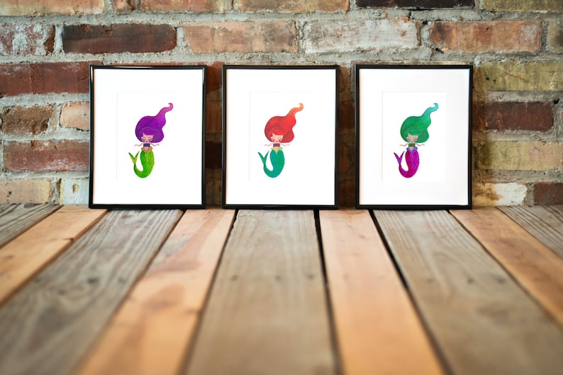 Puede incluir: Tres impresiones enmarcadas de ilustraciones de sirenas. Cada sirena tiene una cola y un cabello de color diferente. Las sirenas sonr&iacute;en todas y tienen los brazos extendidos.
