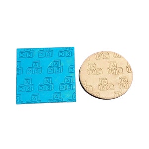 Può includere: Due timbri in silicone con un motivo ripetuto di blocchi di alfabeto impilati. Il timbro a sinistra è blu e il timbro a destra è beige.