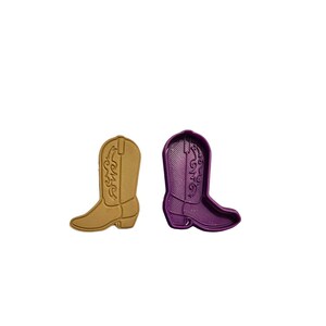May include: Two cowboy boot-shaped cookie cutters. One is a light brown color, and the other is purple. Both have detailed embossed designs of decorative stitching and a pointed toe.