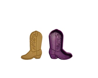 May include: Two cowboy boot-shaped cookie cutters. One is a light brown color, and the other is purple. Both have detailed embossed designs of decorative stitching and a pointed toe.