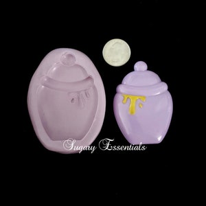 Puede incluir: Un molde de silicona morado y un tarro de miel de resina morado con tapa dorada y miel goteando. El molde es para hacer un tarro de miel.