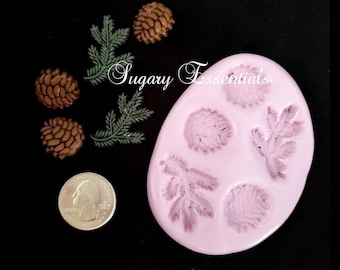 May include: A pink silicone mold with five impressions: two pine cones, two pine branches, and one larger pine cone. The mold is surrounded by four small brown pine cones and two green pine branches.