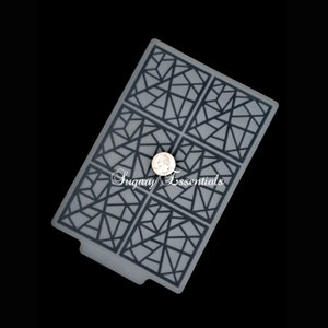 May include: A gray silicone baking mat with a geometric pattern of black lines forming a grid of squares. The text "Sugary Essentials" is printed in white on the mat.