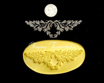 May include: A yellow silicone mold with the design of a decorative wreath with a bow in the center. The mold is oval shaped and has the words "Sugary Essentials" printed on it.
